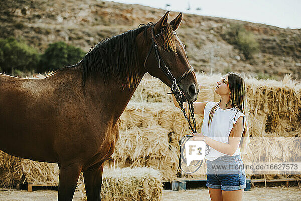 Beautiful young woman holding reins of brown horse