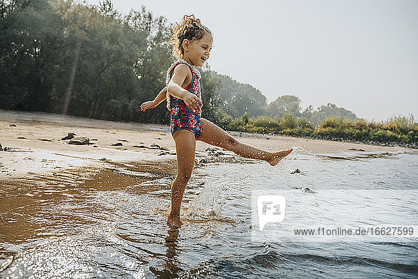 Nettes kleines Mädchen spielt im Wasser am Strand an einem sonnigen Tag