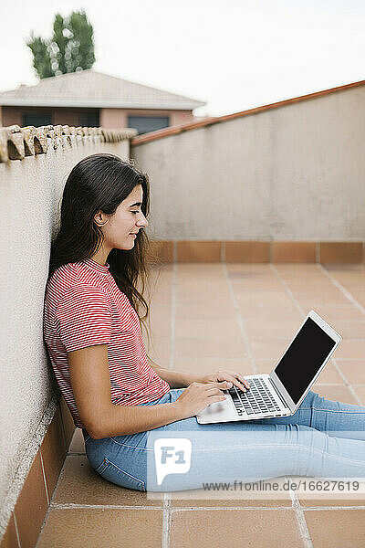 Junge Frau  die auf dem Balkon sitzend am Laptop lernt