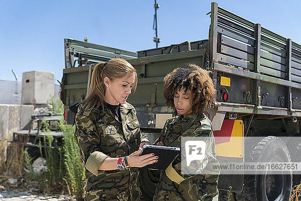 Multiethnische Soldatinnen diskutieren an einem sonnigen Tag in einer Militärbasis über ein digitales Tablet