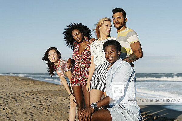 Glückliche junge Freunde stehen am Strand während eines sonnigen Tages