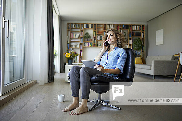 Woman talking on mobile phone while using digital tablet at home