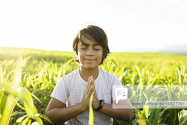 Smiling boy practicing yoga while sitting on grass in meadow