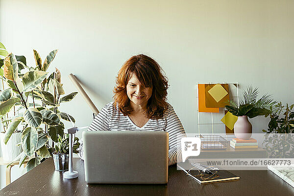 Reife Frau arbeitet am Laptop  während sie zu Hause am Tisch sitzt