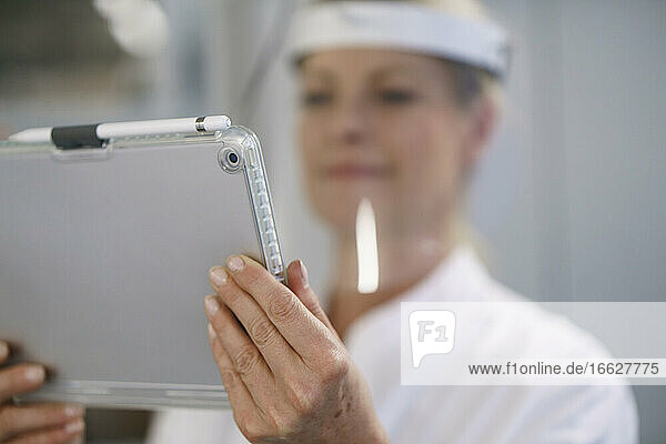 Nahaufnahme einer Wissenschaftlerin mit Gesichtsschutz bei der Arbeit mit einem digitalen Tablet im Labor