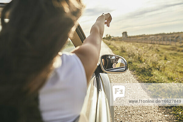 Young woman pointing towards cloudy sky while sitting in car
