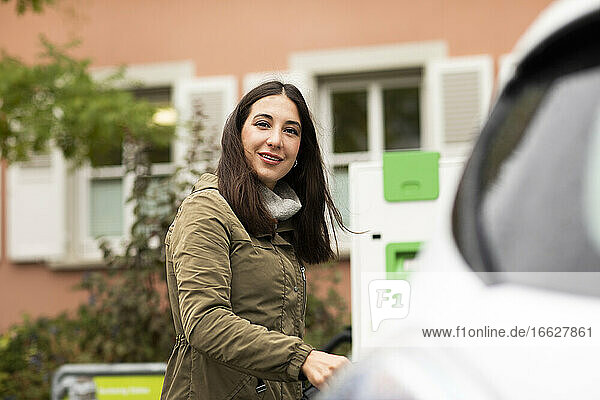 Lächelnde schöne Frau an der Verleihstation für Elektrofahrzeuge