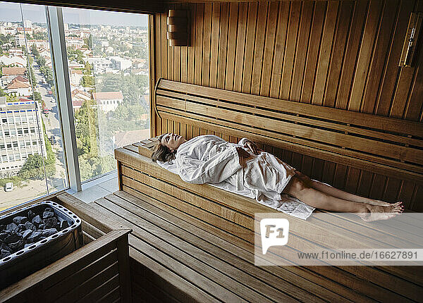Senior woman relaxing in wooden sauna while lying down at health spa