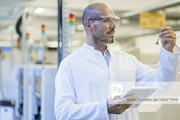 Älterer männlicher Techniker mit Schutzbrille bei der Betrachtung eines Maschinenteils im Labor
