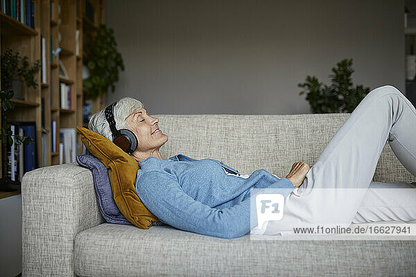 Ältere Frau hört Musik  während sie zu Hause auf dem Sofa liegt