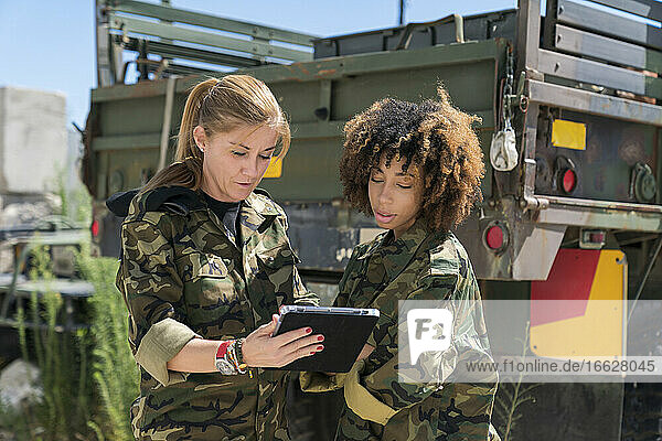 Soldatinnen diskutieren an einem sonnigen Tag über ein digitales Tablet vor einem Lastwagen