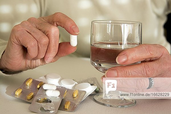 Hände einer älteren Frau mit Tabletten und Wasserglas