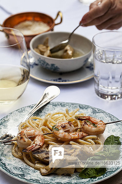 An outdoor table with pasta cacio e pepe (pasta with cheese and pepper)  shrimp skewers with basil  artichokes and white wine