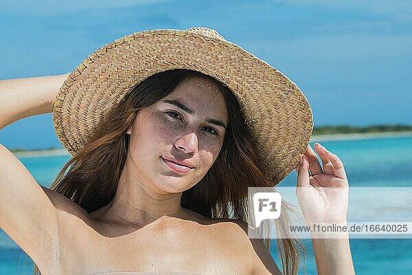 Schöne lateinische Frau im blauen Bikini am tropischen Strand. Porträt der glücklichen jungen Frau gebräuntes Mädchen mit Sonnenhut