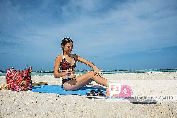 Attraktive junge Frau auf Reisen  am tropischen Strand und mit Sonnencreme.