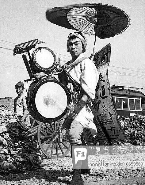 Tokio  Japan  14. Mai 1947.
Eine japanische Ein-Mann-Band und wandelnde Reklame in Form eines Chindonya-Hiromeya   was so viel bedeutet wie Einer  der viele Instrumente spielt und Nachrichten verbreitet .