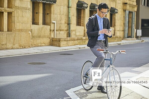 Japanischer Geschäftsmann mittleren Alters  der Fahrrad fährt