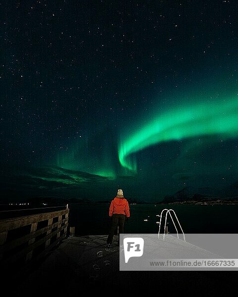 Northern lights over a Norwegian fjord with person in red jacket  Tromsø  Norway  Europe