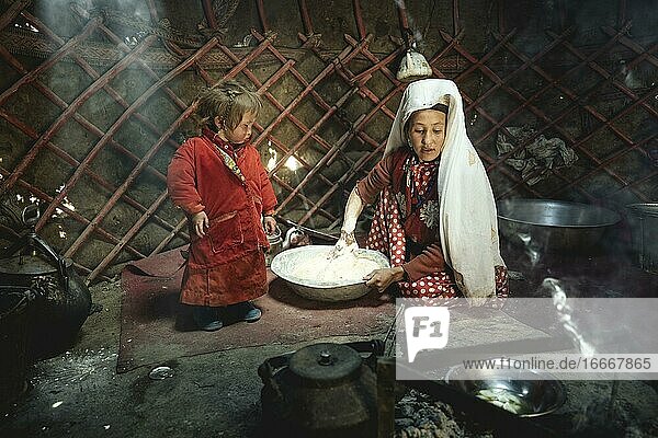 Woman and infant in traditional Kyrgyz traditional traditional traditional traditional traditional traditional traditional traditional traditional costume dough production for flat bread in front of her a teakettle on a fireplace yurt bozai gumbaz wakhan corridor Badakhshan Afghanistan Asia