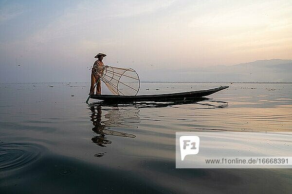 Traditional fisherman posing standing on his small boat in front of sunrise Lake Inle Myanmar Asia