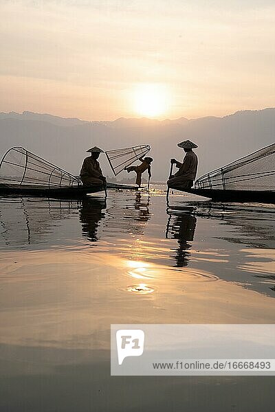 Drei traditionelle Fischer posieren im Stehen und Sitzen auf ihren kleinen Booten vor der Sonnen  Lake Inle  Myanmar  Asien
