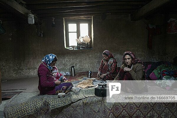 A woman with an infant and two other woman sitting on carpets in the living room of a traditional mud house Khandud Wakhan Corridor Afghanistan Asia