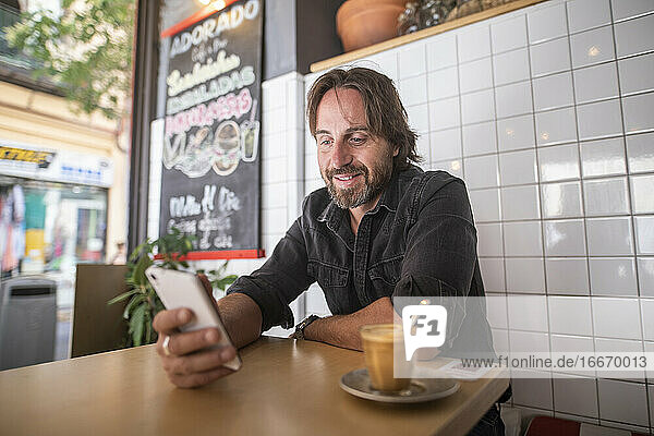 Man enjoying in a coffee shop while looking at the mobile phone