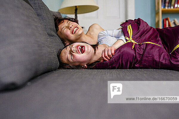 two happy children lay on couch together laughing out loud with joy