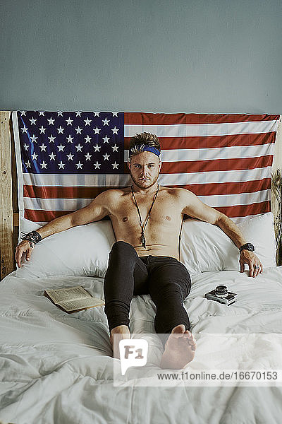 Ein junger Mann im Bett schaut mit der amerikanischen Flagge in die Kamera
