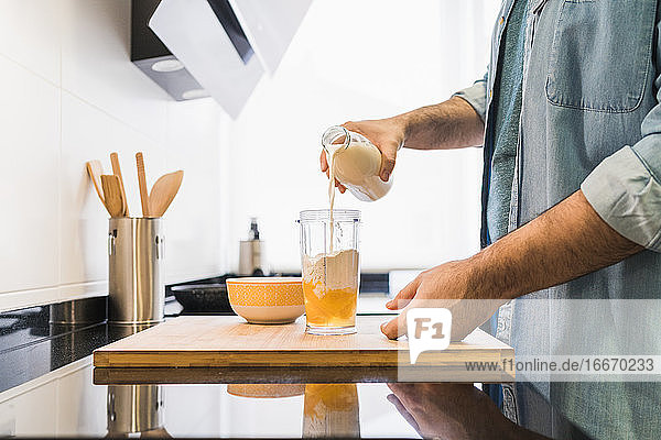 Mann im Jeanshemd beim Kochen in der Küche. Ein anonymer Mann gießt Milch in einen Behälter