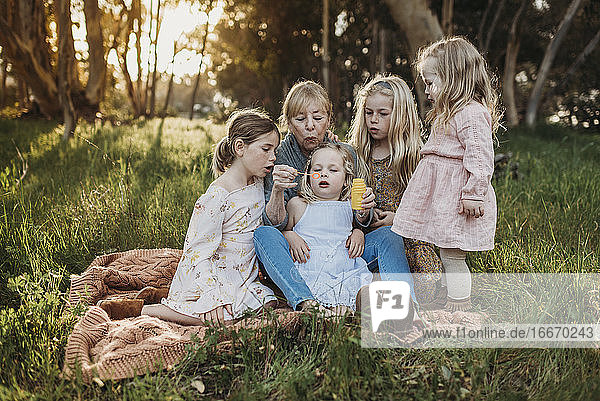 Lifestyle image of grandmother blowing bubbles with granddaughters