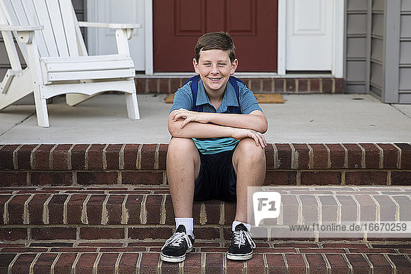 Happy Tween Boy sitzt auf Ziegelstein Front Steps