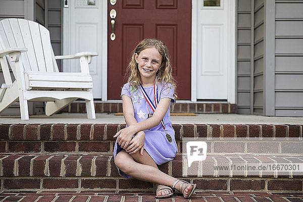 Lächelnd Blonde Mädchen trägt eine Medaille sitzt auf Front Brick Front Steps