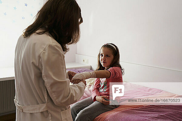 Seitenansicht einer Ärztin  die den Arm eines kleinen Mädchens in ihrem Zimmer verbindet. Hausarzt Konzept