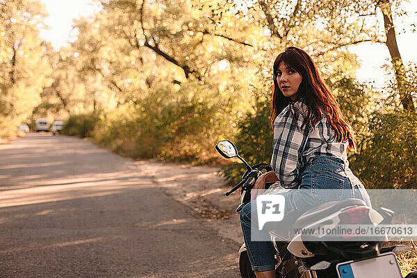 Young woman looking over shoulder while sitting on motorcycle on road