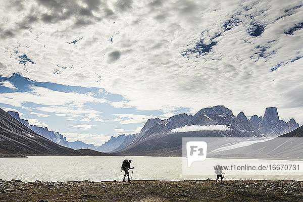 Silhouettierte Rucksacktouristen wandern am Ufer eines Bergsees entlang.