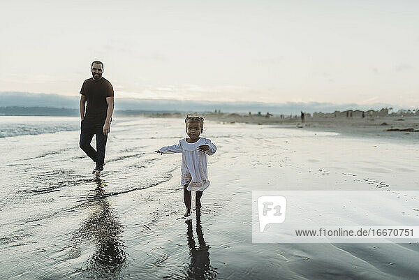 Junges Kleinkind Mädchen läuft am Strand mit Papa im Meer