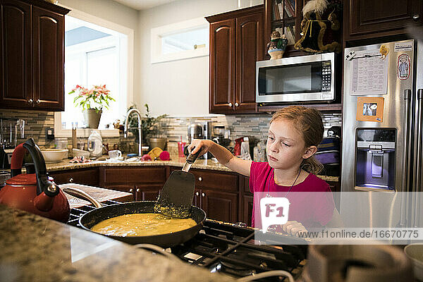 Candid Image of Unsmiling Young Girl Cooking Eggs In Messy Kitchen