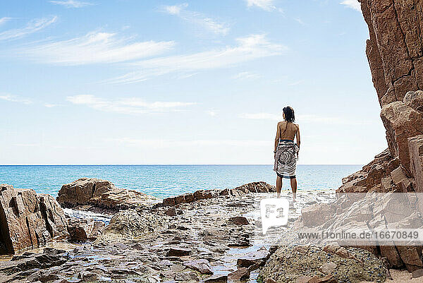 Rückansicht einer Frau  die am Meer steht und zum Horizont blickt