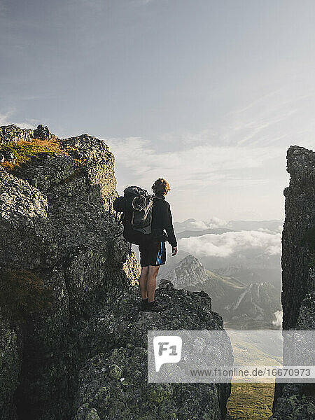 Junger Mann mit Rucksack steht an einer Klippe und starrt in die Landschaft