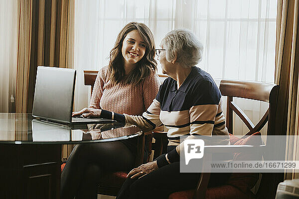 granddaughter and grandmother smile while using laptop