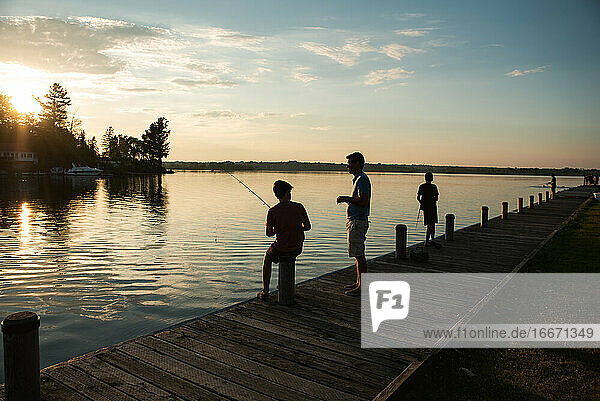 Father and sons fishing on dock of lake at sunset in Ontario  Canada.