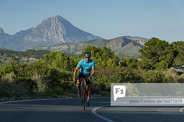 Ein Mann  der sich auf die Pedale stellt  fährt auf der Straße von Alicante bergauf