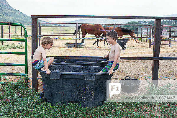 Geschwister spielen an einem heißen Tag im Wasser für Pferde