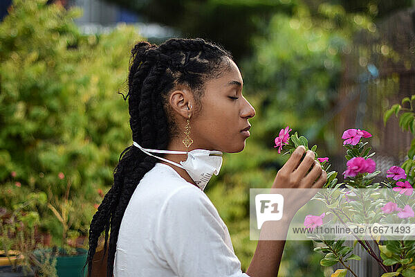 Junge Frau nimmt Gesichtsmaske ab  um an den Blumen zu riechen