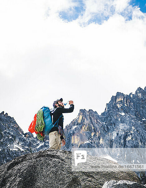 Mann trinkt Wasser auf Klettertour mit Bergen im Hintergrund
