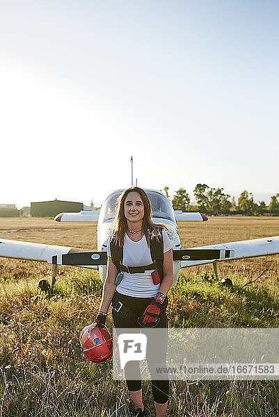 Junge Fallschirmspringerin auf einem Flugplatz mit einem Flugzeug hinter ihr