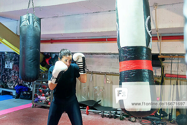 Weiblicher Boxer  der in einem Boxstudio auf einen riesigen Sandsack einschlägt.