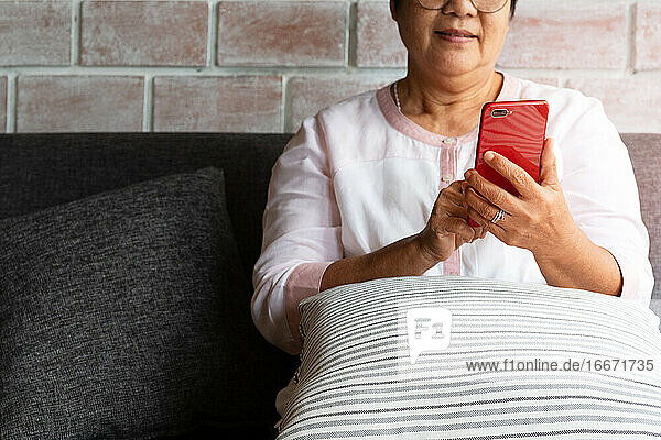 ältere Frau  die ein Mobiltelefon benutzt  während sie zu Hause auf dem Sofa sitzt
