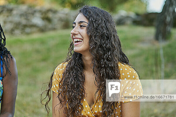 Junge Frau mit Locken lächelt in einem Park und trägt eine gelbe Bluse
